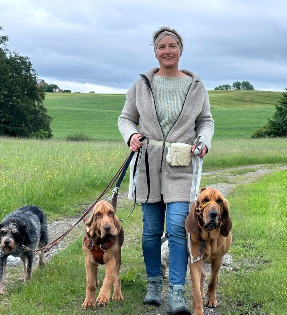 Sandra Mendler geht mit drei Hunden an lockerer Leine über einen Feldweg im Allgäu