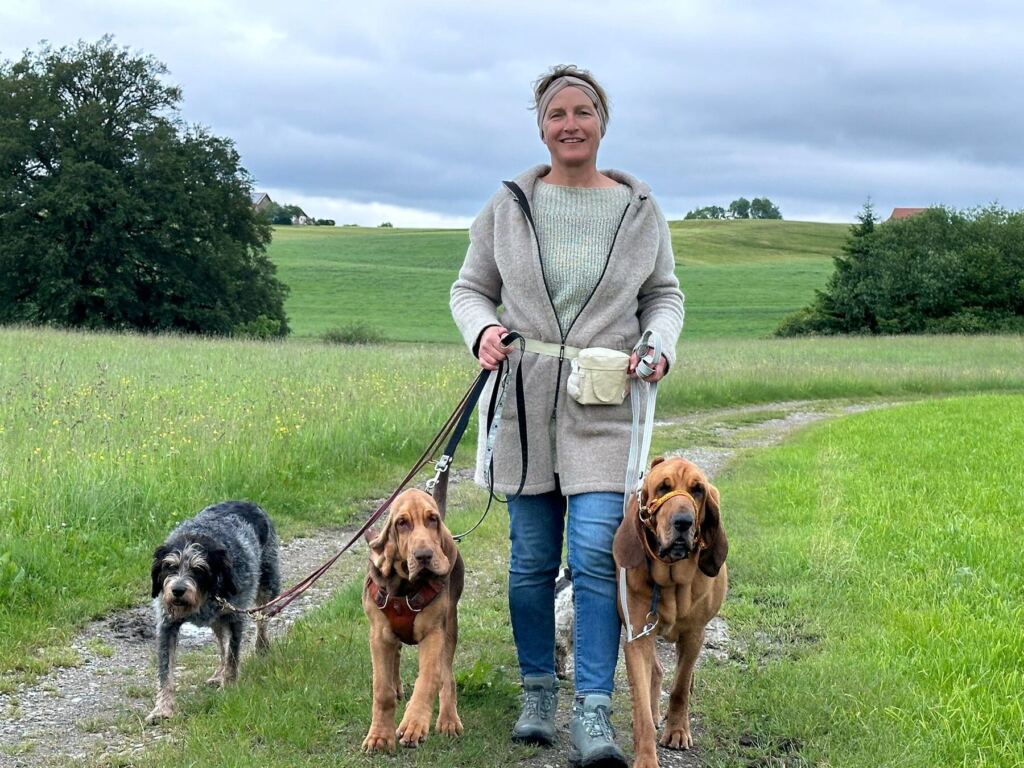 Sandra Mendler geht mit drei Hunden an lockerer Leine über einen Feldweg im Allgäu