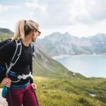 Wanderin mit Rucksack blickt über einen Bergsee in den Alpen