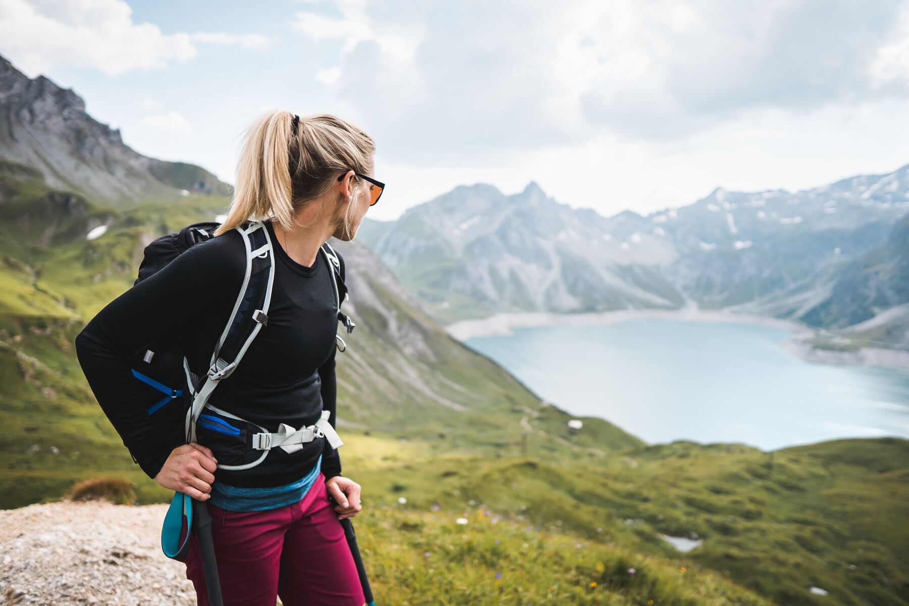 Wanderin mit Rucksack blickt über einen Bergsee in den Alpen